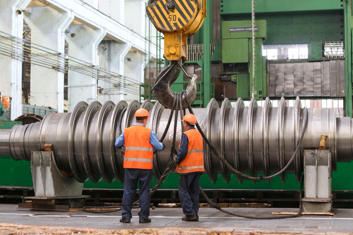 Two workers in hi-vis guiding a lifted machine part